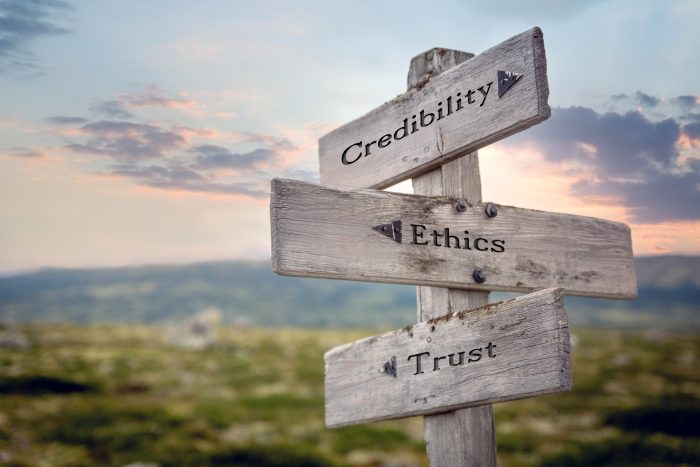 credibility ethics trust text quote on wooden signpost outdoors during sunset.